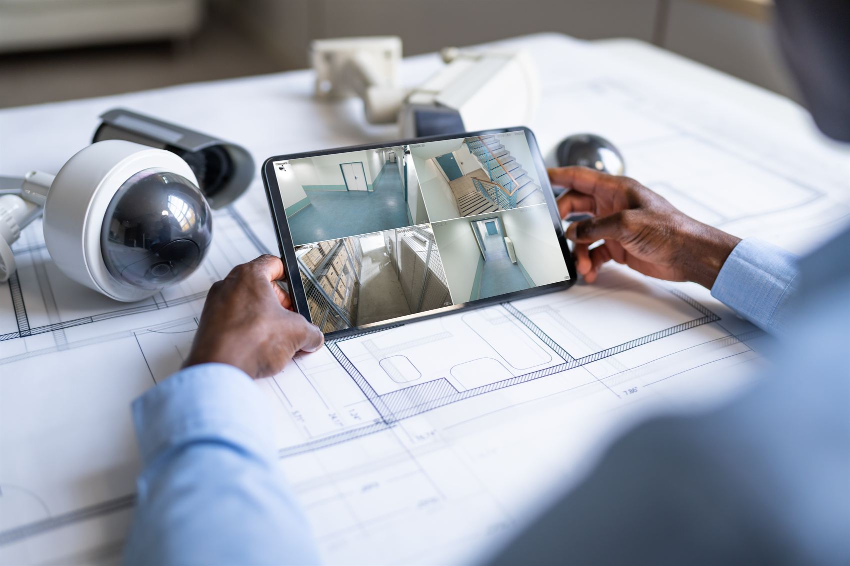 Multiple security camera feeds monitored on a tablet next to dome cameras and building plans